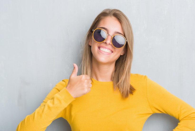 Beautiful Young Woman Standing over Grunge Grey Wall Wearing Retro Sunglasses Happy with Big Smile Doing Ok Sign Thumb Up with Fingers Excellent Sign Flurl how to make the coolest sunglasses look even cooler